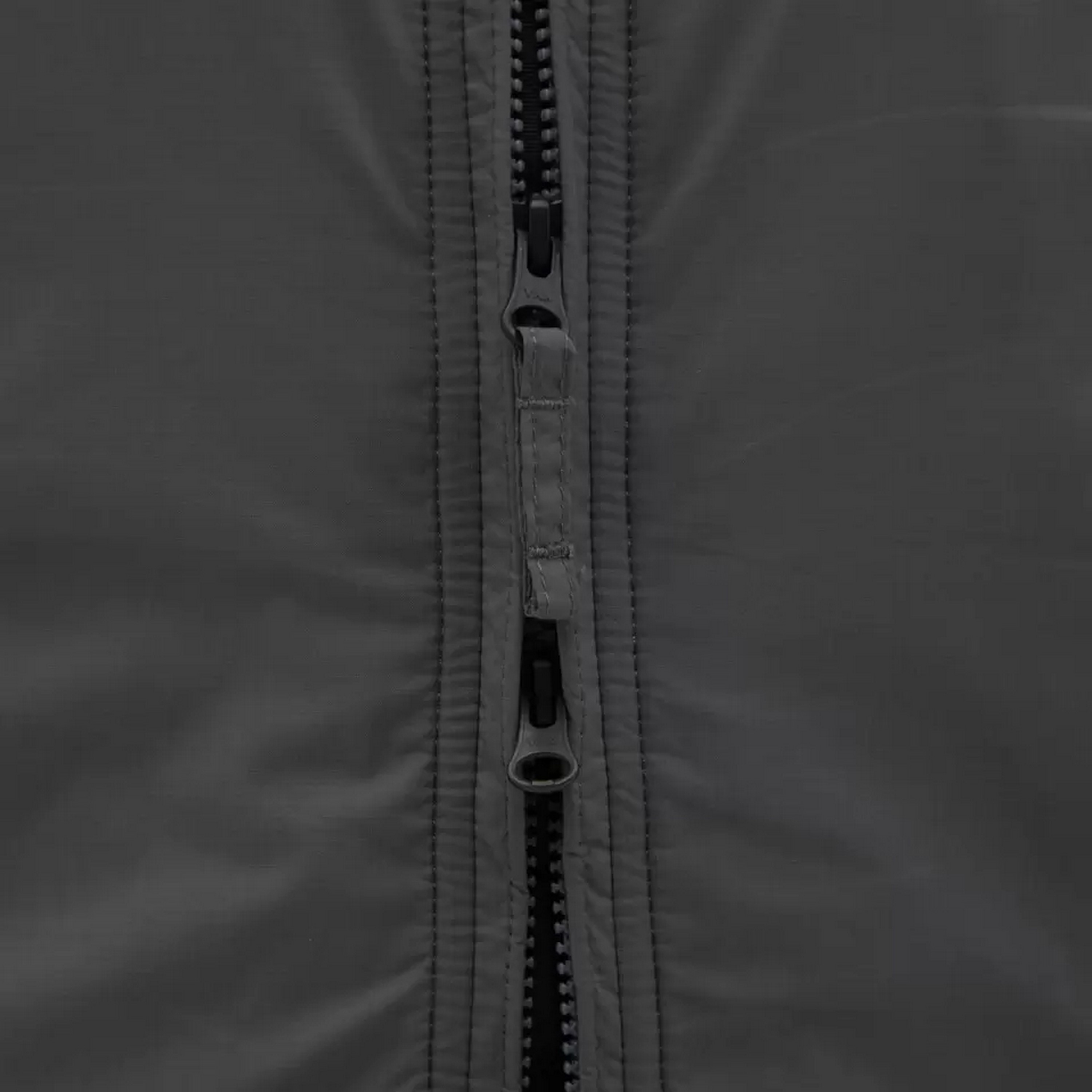 Nahaufnahme eines grauen Reißverschlusses einer taktischen Jacke mit zwei Zuglaschen, die eine robuste Stoffkonstruktion für Notfallausrüstung zeigt.