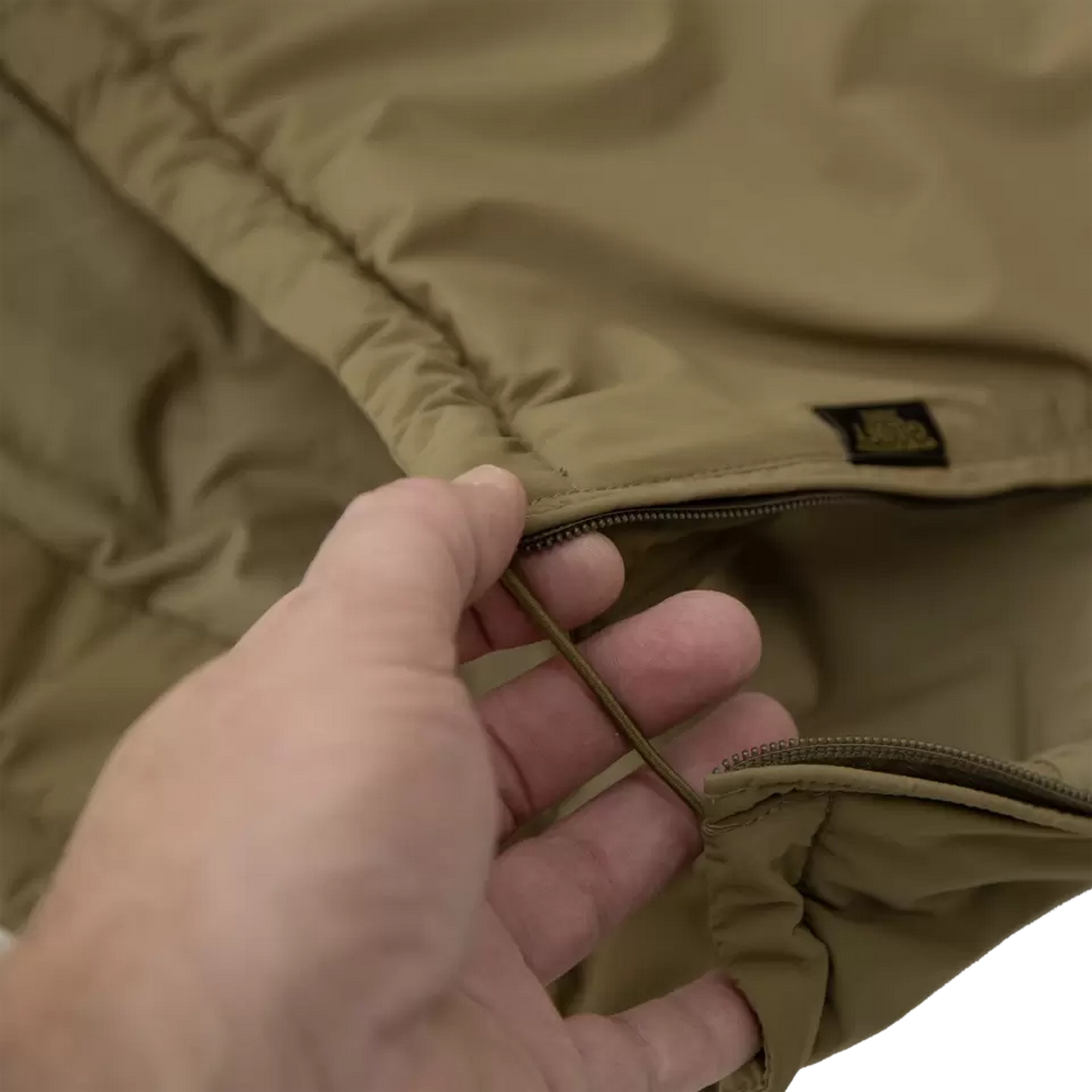 Nahaufnahme einer Hand, die den Reißverschlussschieber an einer hellbraunen Tasche für taktische Ausrüstung hält, zeigt strapazierfähigen Stoff und hochwertige Konstruktion.