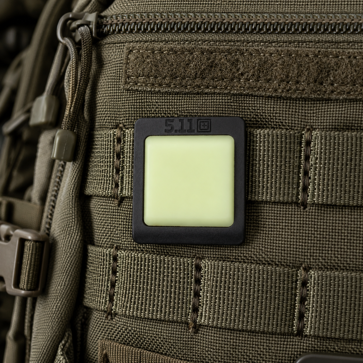 Ein im Dunkeln leuchtendes 5.11 Tactical-Moral-Patch, das am MOLLE-Gurtband einer olivfarbenen taktischen Ausrüstungstasche befestigt ist.